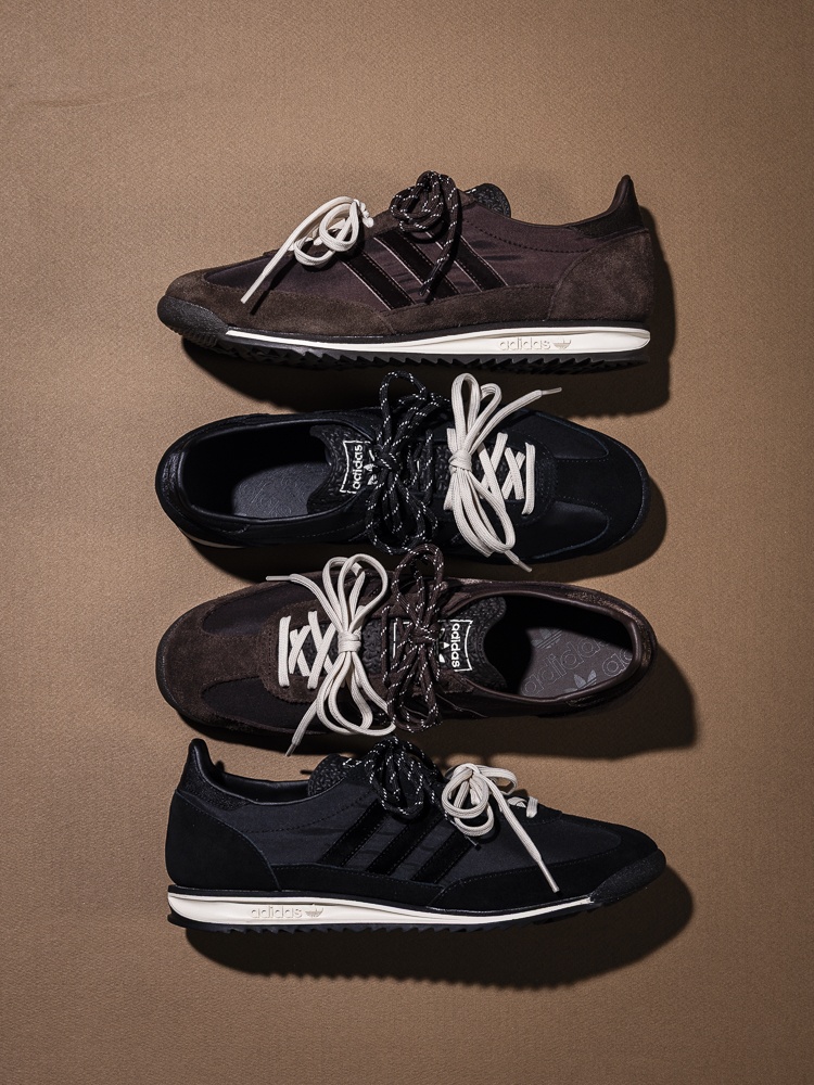 A stack of dark-colored, lace-up sneakers or athletic shoes against a plain, beige background.