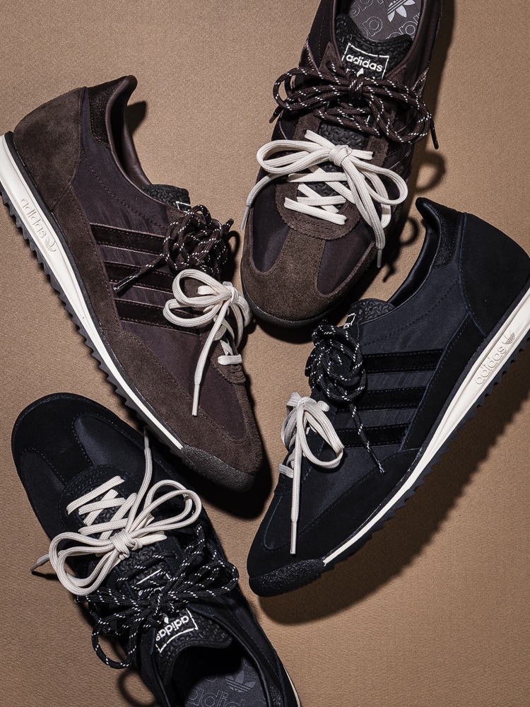 A pair of dark-colored athletic shoes with white laces and accents, set against a plain beige background.