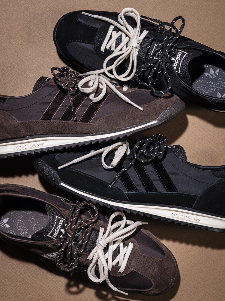 A pair of black and white Adidas sneakers with laces and intricate designs, resting on a beige background.