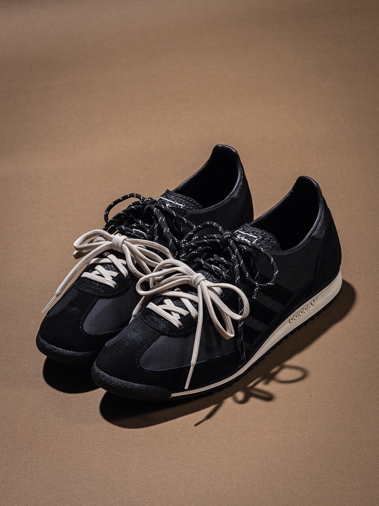 A pair of black sneakers with laces sits on a plain, beige background.