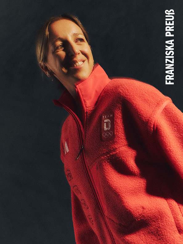 Eine Person, die eine leuchtend rote Jacke trägt, lächelt vor einem dunklen Hintergrund.