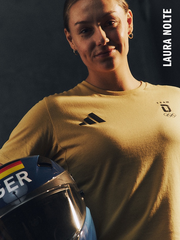 Eine lächelnde Person, die ein gelbes Trikot trägt und einen Motorradhelm in der Hand hält.