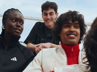 Tres jóvenes, dos hombres y una mujer, están de pie juntos y sonrientes en un entorno al aire libre con un cielo despejado de fondo.