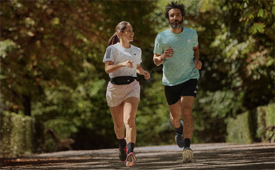 A man and a woman are jogging together on a path surrounded by lush greenery.