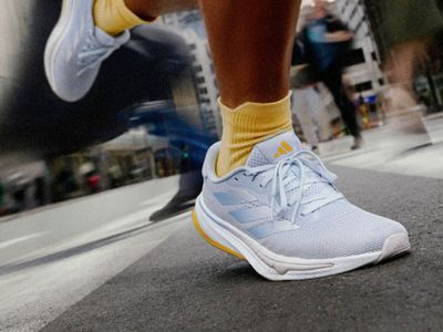 Dół osoby w białych sneakerach i żółtych skarpetkach, stojącej na ulicy z rozmytymi elementami tła.