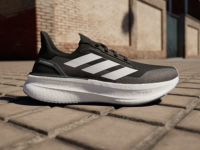 Ett par svarta och vita adidassneakers vilar på en tegelyta, med en tegelvägg synlig i bakgrunden.