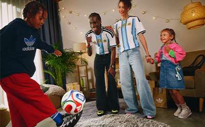 A group of people, including children, are gathered in a room decorated with festive lights, with a soccer ball in the foreground.