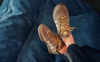 The image shows a pair of beige athletic shoes with orange accents, resting on a blue fabric surface.
