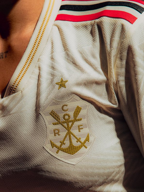The image shows a close-up view of a white sports jersey or uniform with a gold anchor and star emblem, along with colorful striped patterns on the sleeves.