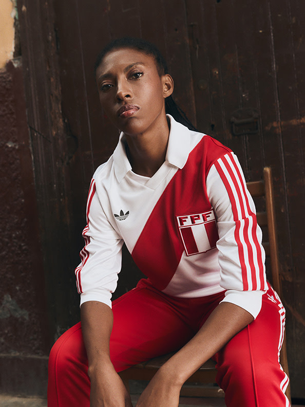 A young person wearing a red and white sports jersey sits against a weathered wooden wall in the background.