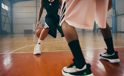 The image shows a person wearing a black athletic outfit and sneakers, standing on a basketball court with a basketball in their hands.