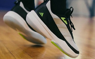 A pair of white and black athletic shoes with neon green accents sit on a wooden surface, against a blurred background.