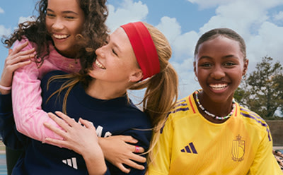 Two young women with diverse backgrounds are embracing and smiling joyfully in an outdoor setting with a cloudy sky in the background.
