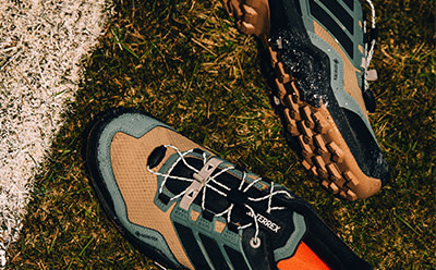 A pair of hiking boots with a vibrant orange sole rests on a grassy surface, surrounded by a natural, earthy background.
