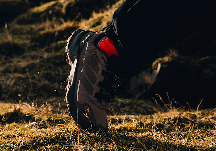 A person wearing a black backpack stands in a grassy field, with a warm, golden light illuminating the scene in the background.