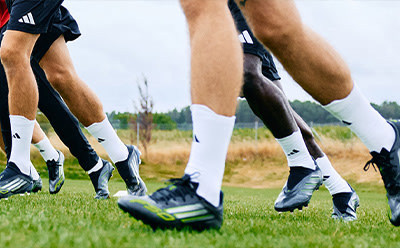 The image shows the lower body of two soccer players wearing cleats and uniforms on a grassy field.