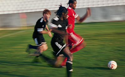 Two figures in motion, one in a red uniform and the other in black, engaged in a dynamic soccer match on a grassy field.