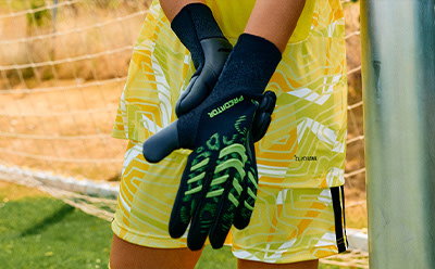 A pair of black and green sports gloves against a blurred yellow and green background, suggesting an athletic or outdoor setting.