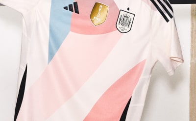 Un maillot de football blanc et rose orné du logo adidas et d'un blason de l'équipe nationale sur un fond clair.