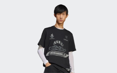 Un joven con una camiseta negra con varios logotipos y gráficos destaca sobre un fondo blanco liso.