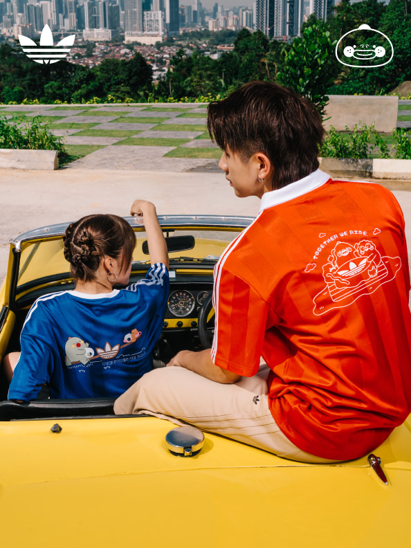 Two young individuals, a boy and a girl, are seated in a yellow car in the foreground, with a cityscape visible in the background.