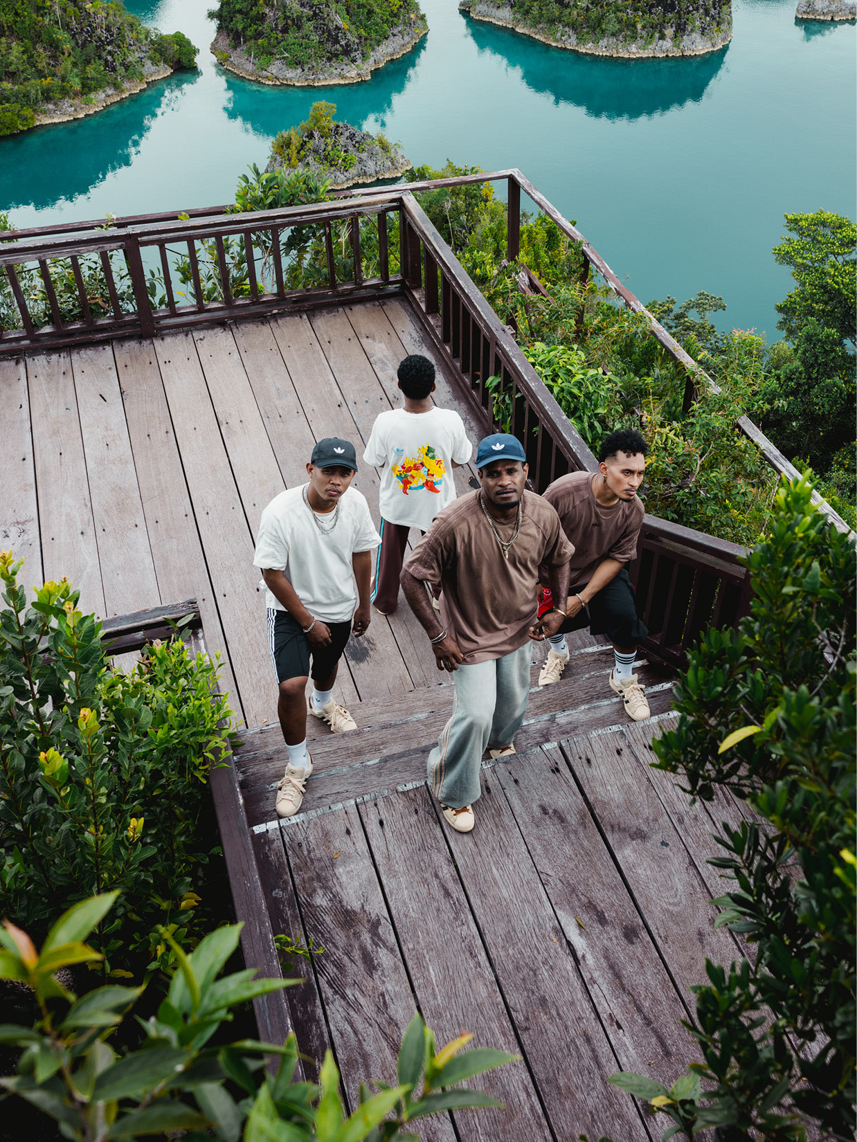 A group of people walking on a wooden deck overlooking a scenic turquoise lagoon surrounded by lush, verdant vegetation.