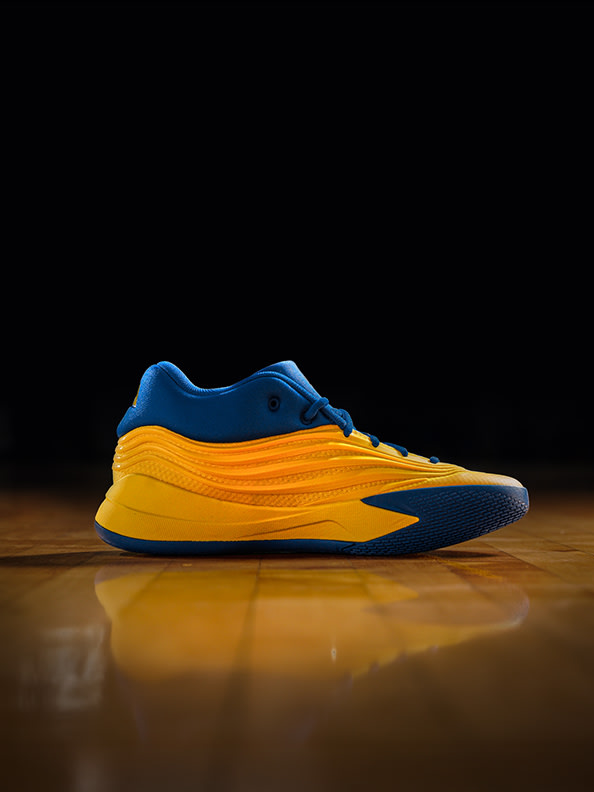 A vibrant blue and yellow sneaker rests on a reflective wooden surface against a dark background.