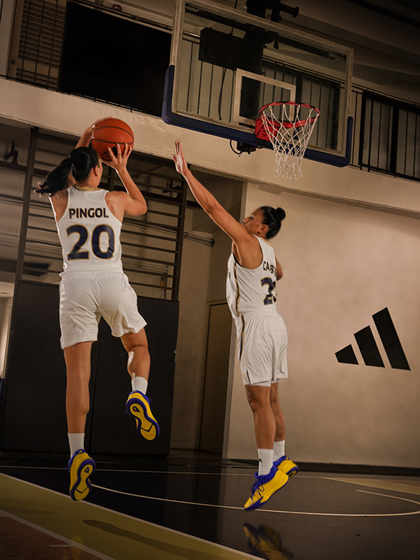 Two basketball players in white jerseys are competing for the ball near the basketball hoop in an indoor court setting.