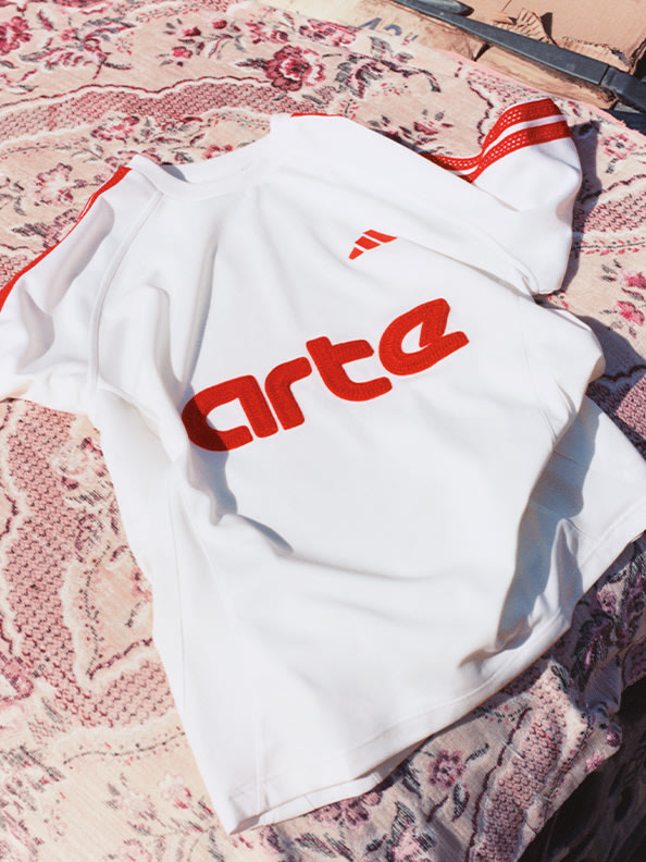 A white sweatshirt with the word "Arta" printed in red lies on a patterned rug or blanket.