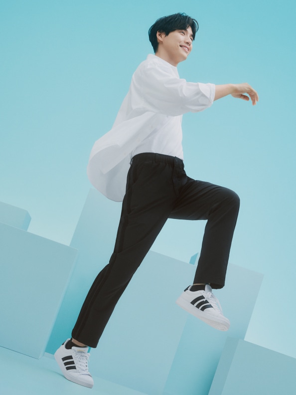 A person in a white shirt and black pants is jumping against a bright blue background.