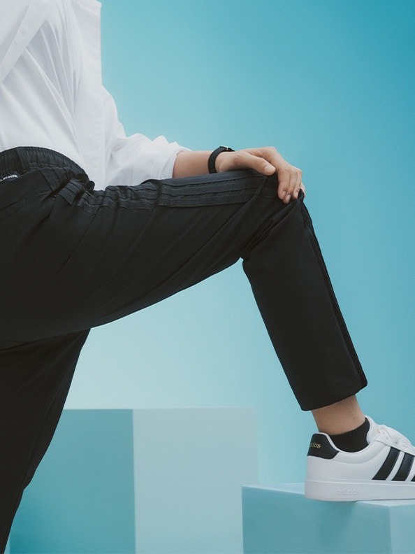 A person's lower body wearing black pants and white sneakers, against a bright blue sky background.