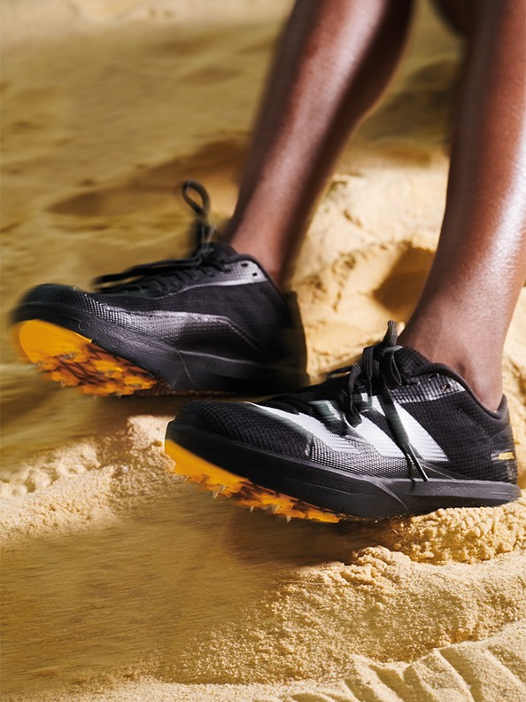 L'image montre une paire de chaussures de sport grises et orange avec le logo adidas sur le côté, reposant sur une surface bleue et blanche.