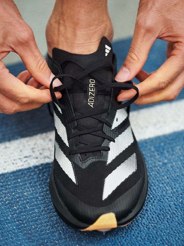 L'image montre une paire de mains nouant les lacets d'une chaussure de sport noire et blanche sur une surface bleue.