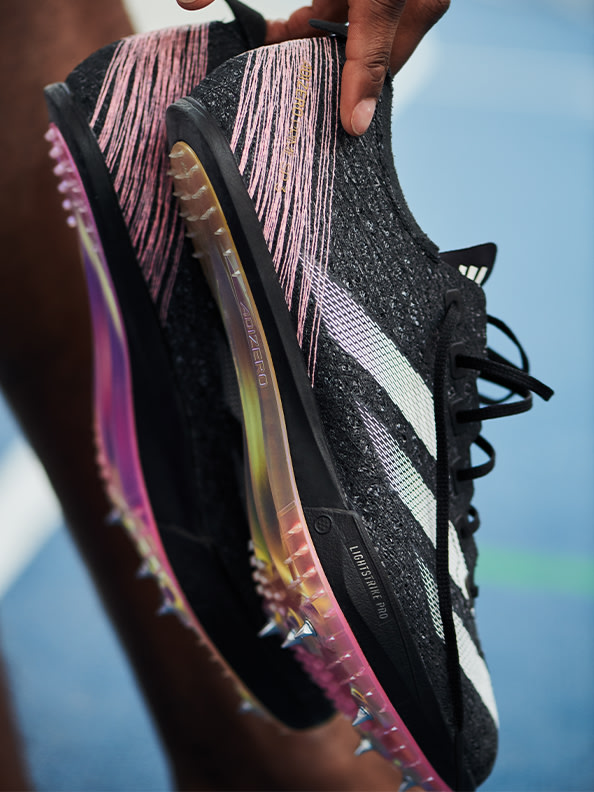 Gros plan sur une paire de chaussures de sport noires et roses au design irisé texturé, sur un fond flou et coloré.