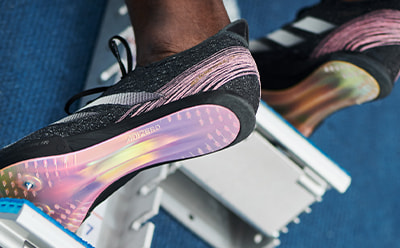 L'image montre en gros plan une paire de sneakers colorées au look futuriste, avec une semelle irisée flashy et une tige noire stylée.