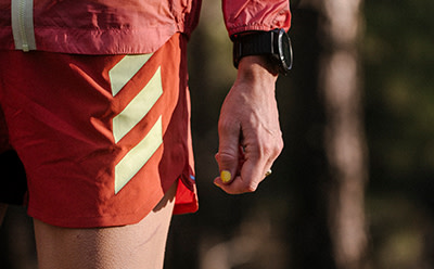 Eine Person, die eine leuchtend rot-orangefarbene Jacke trägt, mit einer sichtbaren Hand, die ein Gerät vor einem dunklen Hintergrund hält.
