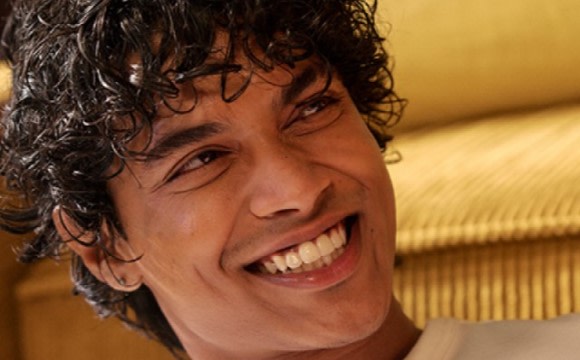 A smiling young man with curly dark hair against a warm-toned background.