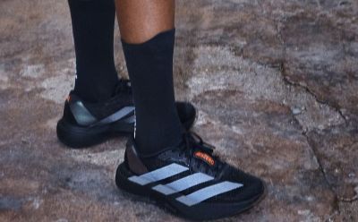 The image shows a person's legs and feet wearing black athletic shoes on a rocky, outdoor surface.