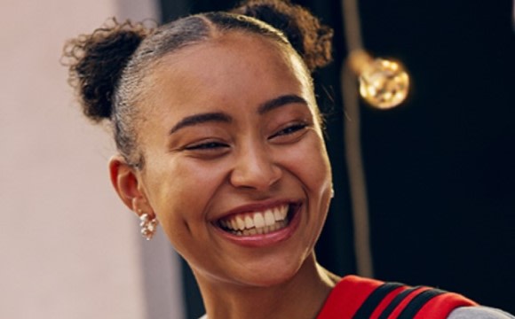 A smiling woman with curly hair and gold earrings, against a dark background.