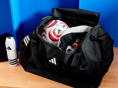 A black sports bag filled with various sports equipment, including a soccer ball, against a vibrant blue background.
