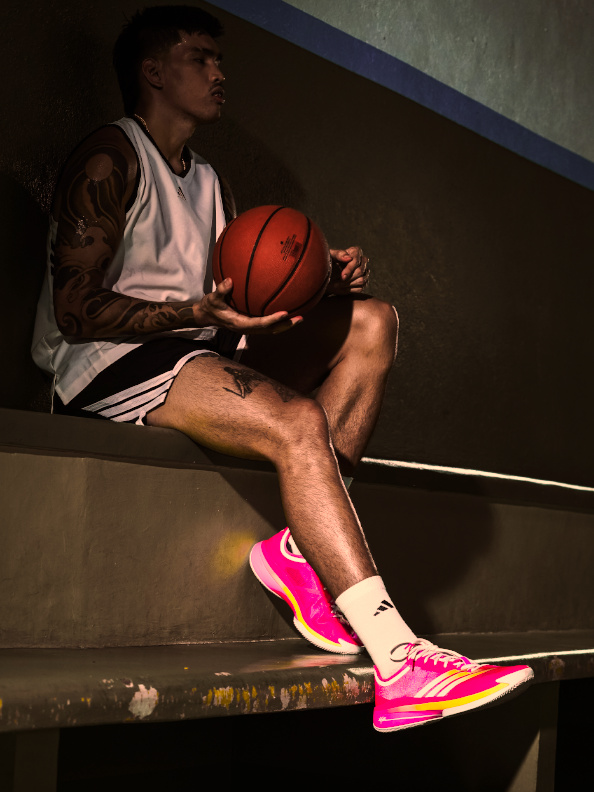 A person in athletic clothing sits on a bench, holding a basketball and wearing bright pink sneakers.