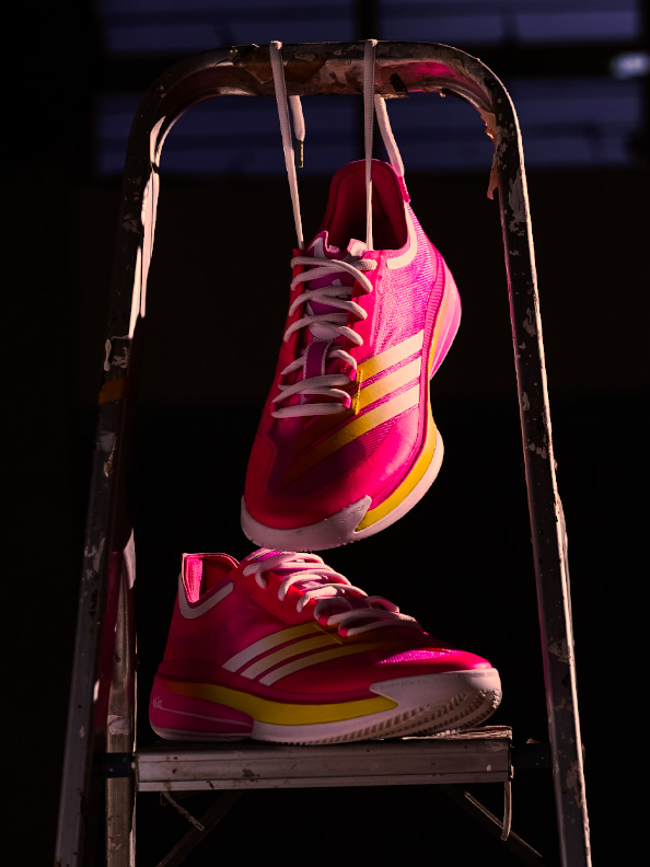 The image shows a pair of vibrant, neon-colored athletic shoes suspended on a metal rack against a dark background.
