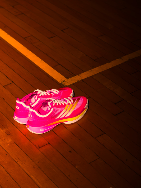 A vibrant pink and orange athletic shoe rests on a wooden floor, casting a warm glow in the dimly lit environment.