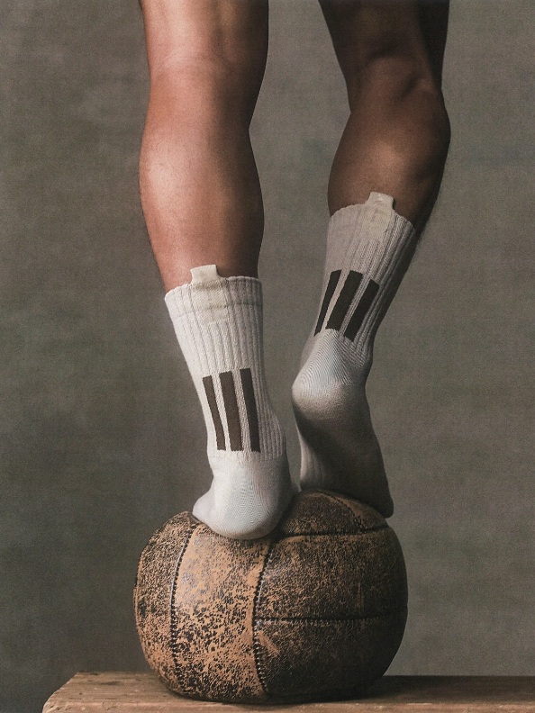 The image depicts a pair of legs standing on a large, rough-textured rock or stone, with the person wearing white athletic socks with black stripes.