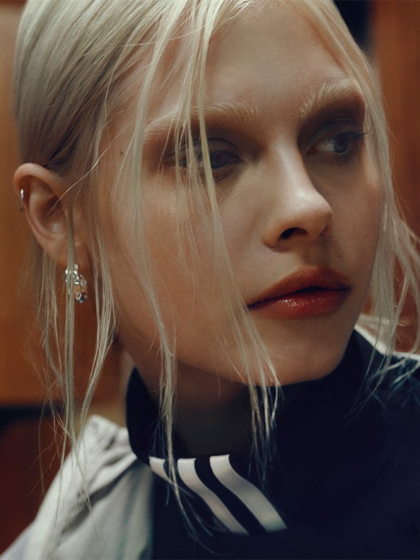 The image depicts a close-up portrait of a young woman with striking blonde hair and piercing blue eyes, set against a dark background.