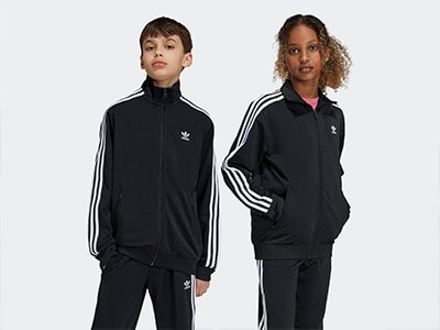 Two individuals wearing black Adidas tracksuits with white stripes stand against a plain white background.