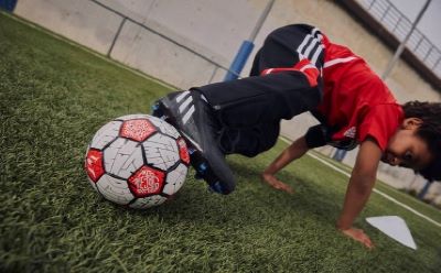 A person in a red jersey is kneeling on a grassy field, reaching for a soccer ball.