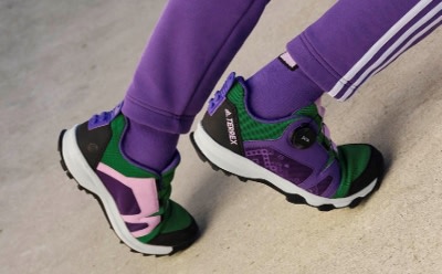 The image shows a pair of colorful sneakers with a purple, green, and black design, resting on a light-colored surface.