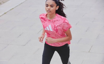 A young woman wearing a vibrant pink and white athletic top stands against a plain white background, her expression focused and determined.