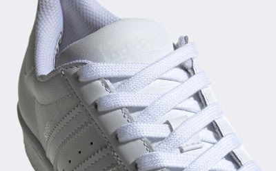 Nahaufnahme eines weißen Sneakers mit Schnürsenkeln und strukturierter Sohle vor einem weißen Hintergrund.